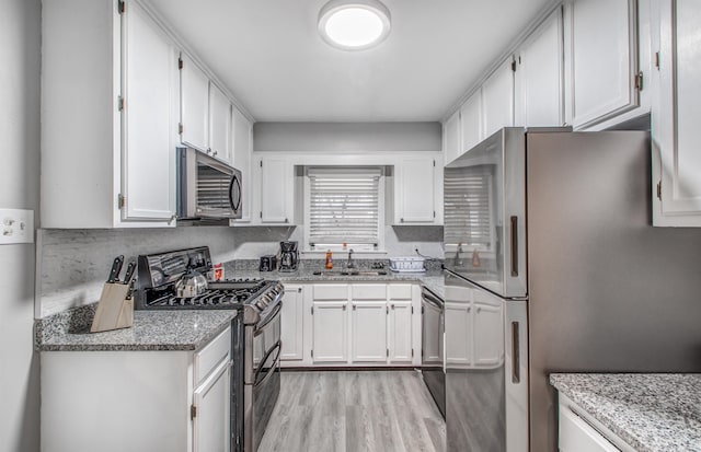 kitchen with light stone countertops, stainless steel appliances, white cabinetry, and sink