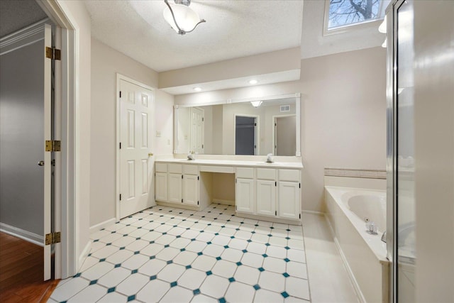 bathroom featuring a tub to relax in, vanity, and a textured ceiling