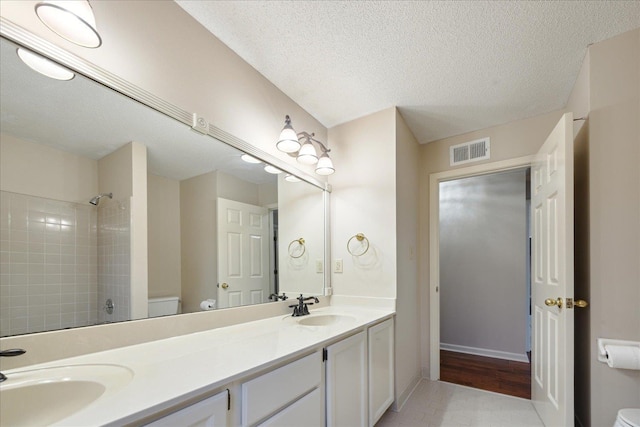 bathroom featuring tile patterned floors, a tile shower, a textured ceiling, vanity, and toilet