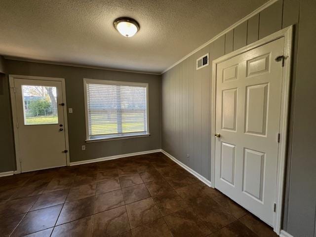 entryway featuring crown molding, wooden walls, dark tile patterned floors, and a textured ceiling