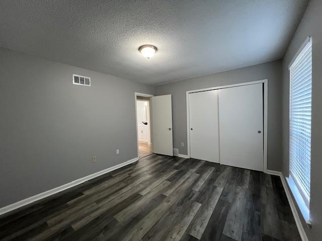 unfurnished bedroom with a textured ceiling, dark hardwood / wood-style flooring, and a closet