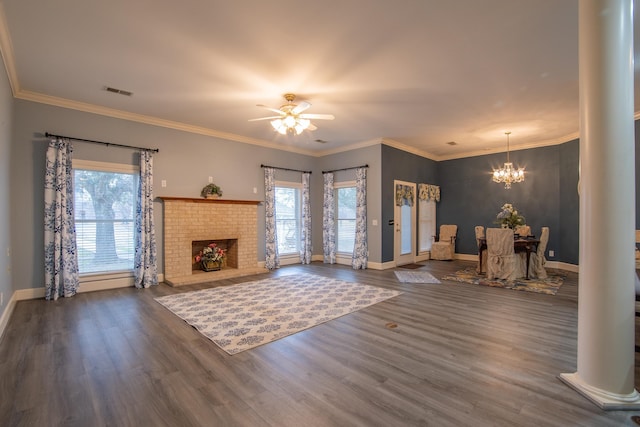 living room featuring ceiling fan with notable chandelier, a brick fireplace, ornamental molding, dark hardwood / wood-style flooring, and decorative columns