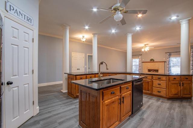 kitchen featuring ornate columns, a kitchen island with sink, sink, dishwasher, and light hardwood / wood-style floors