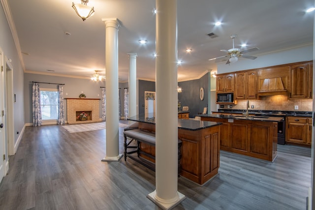 kitchen with black microwave, decorative columns, crown molding, hardwood / wood-style floors, and a center island with sink