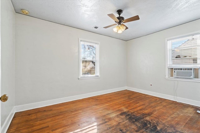 spare room featuring hardwood / wood-style floors, cooling unit, a textured ceiling, and a wealth of natural light