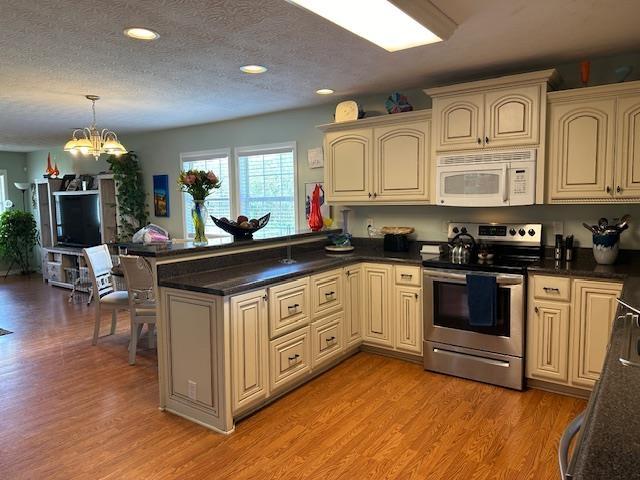 kitchen featuring kitchen peninsula, light hardwood / wood-style flooring, a notable chandelier, stainless steel electric range oven, and hanging light fixtures