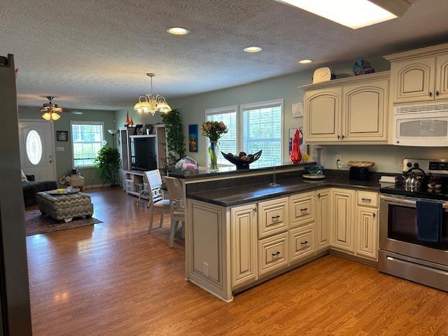 kitchen with light hardwood / wood-style flooring, kitchen peninsula, a textured ceiling, electric stove, and ceiling fan with notable chandelier