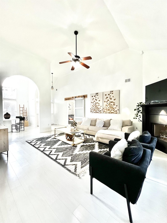 living room featuring ceiling fan, a barn door, and high vaulted ceiling