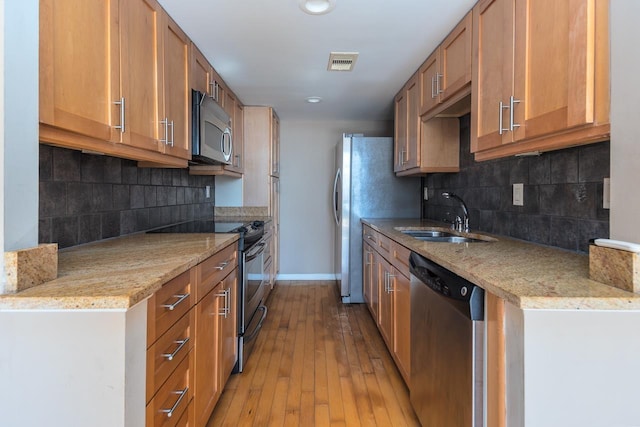 kitchen with stainless steel appliances, light stone countertops, light hardwood / wood-style floors, and sink