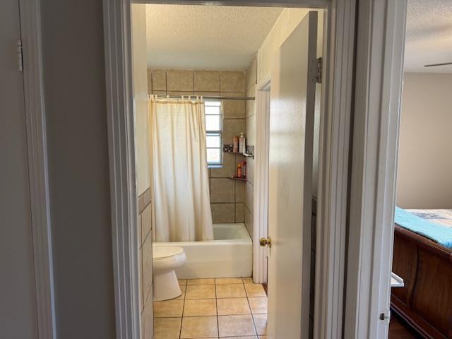 bathroom featuring tile patterned floors, shower / bath combination with curtain, toilet, and a textured ceiling