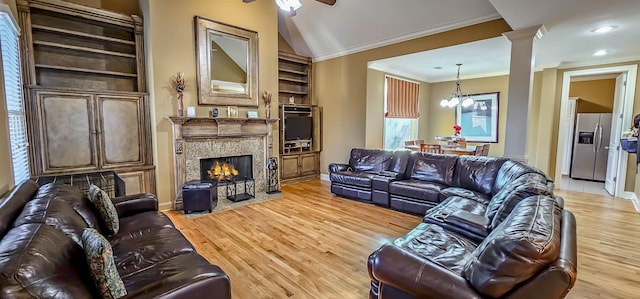 living room with light wood-type flooring, decorative columns, ceiling fan with notable chandelier, vaulted ceiling, and crown molding