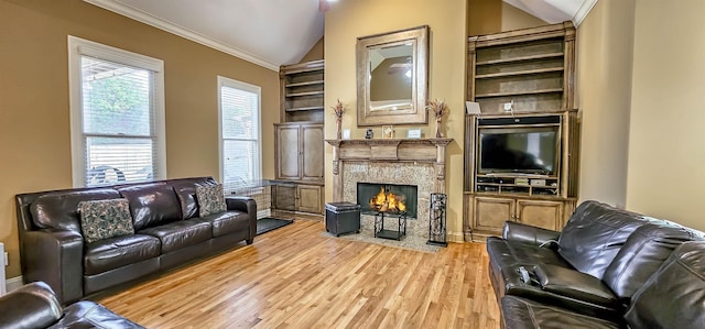 living room featuring a stone fireplace, crown molding, vaulted ceiling, built in features, and light hardwood / wood-style floors