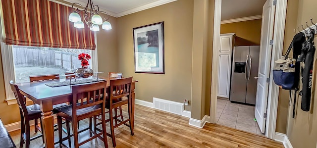 dining space with light wood-type flooring, ornamental molding, and a chandelier