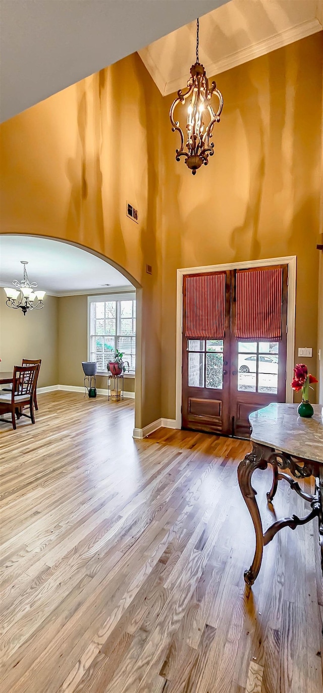 foyer featuring wood-type flooring, a towering ceiling, crown molding, and a notable chandelier