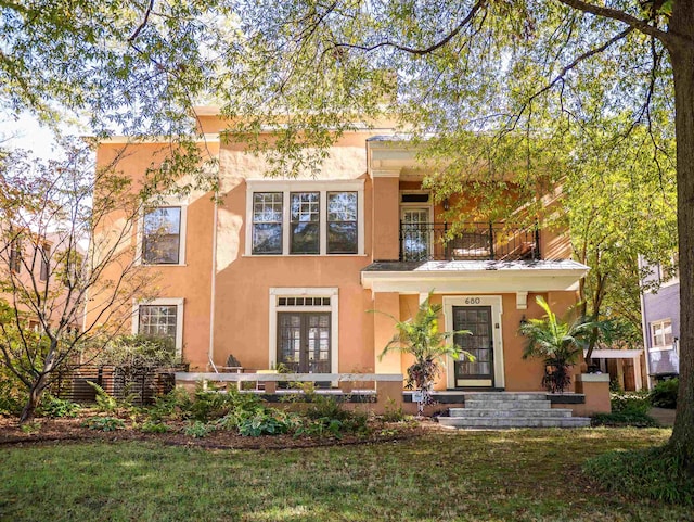 view of front of home featuring a front lawn, a balcony, and french doors