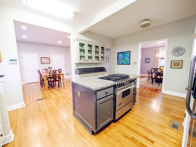 kitchen featuring gray cabinetry, a center island, stainless steel stove, light hardwood / wood-style flooring, and white cabinets