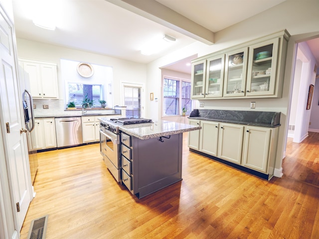 kitchen with dark stone countertops, light wood-type flooring, beam ceiling, appliances with stainless steel finishes, and a kitchen island