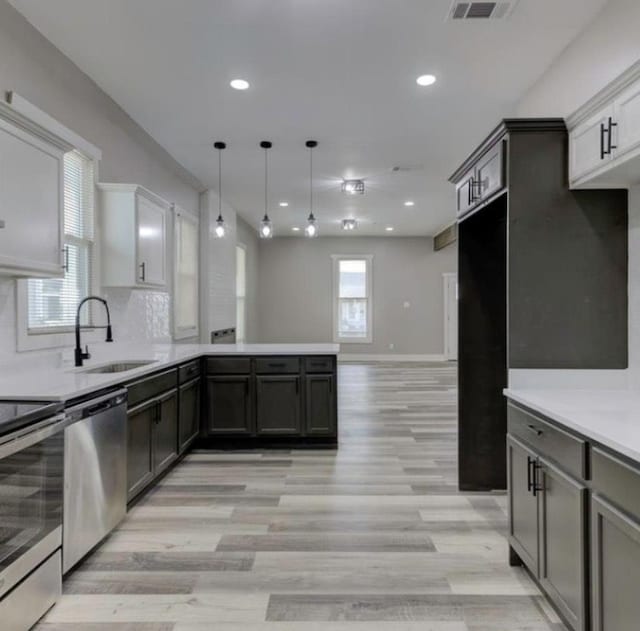 kitchen with kitchen peninsula, appliances with stainless steel finishes, sink, white cabinetry, and hanging light fixtures