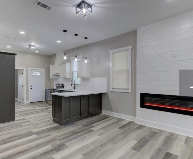 kitchen featuring white cabinetry, sink, kitchen peninsula, a fireplace, and stainless steel range with electric cooktop