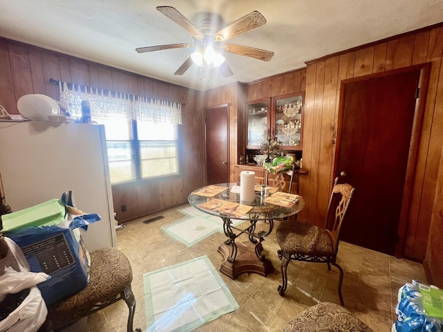 dining space featuring ceiling fan and wooden walls