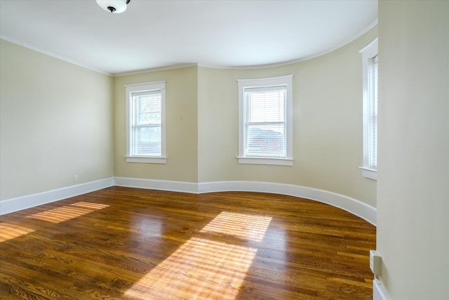 empty room featuring plenty of natural light, dark wood-type flooring, and ornamental molding