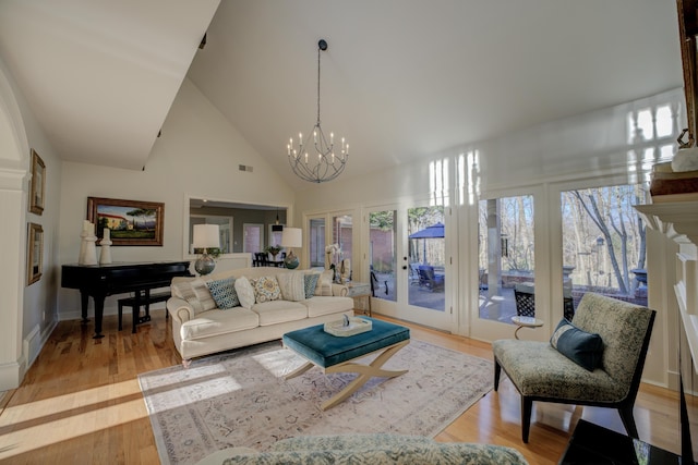 living room with a notable chandelier, light hardwood / wood-style floors, and high vaulted ceiling