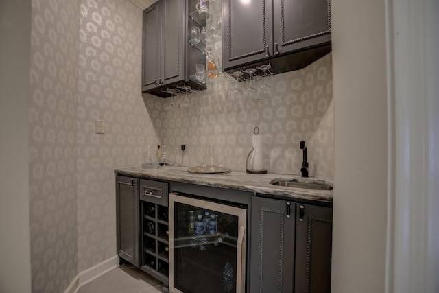 bar featuring gray cabinetry, sink, beverage cooler, light stone counters, and light tile patterned floors