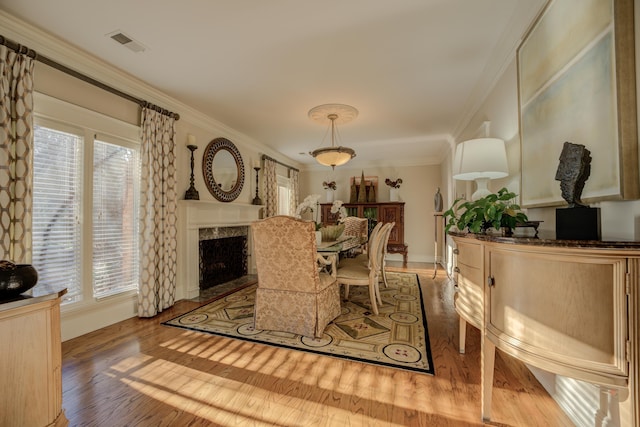 dining area featuring ornamental molding, a high end fireplace, a healthy amount of sunlight, and light wood-type flooring