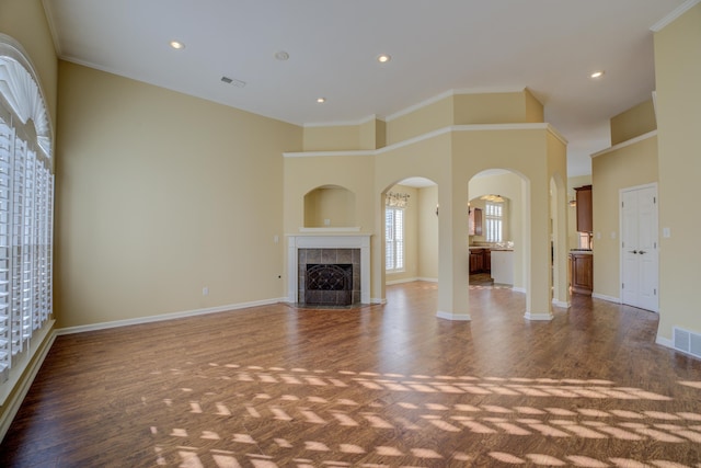 unfurnished living room featuring a tile fireplace, dark wood-type flooring, a high ceiling, and ornamental molding