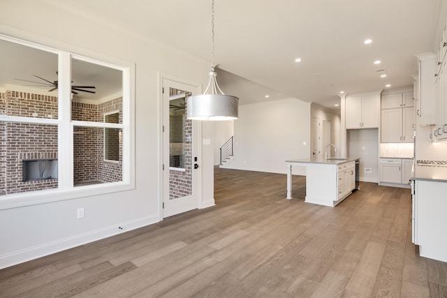 kitchen featuring sink, hanging light fixtures, crown molding, light hardwood / wood-style floors, and a center island with sink