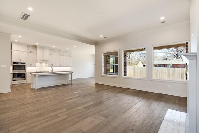 unfurnished living room with hardwood / wood-style floors, plenty of natural light, and crown molding