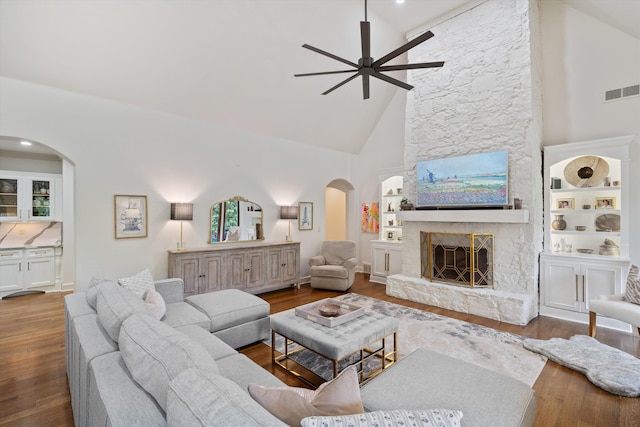 living room with high vaulted ceiling, a stone fireplace, ceiling fan, built in features, and wood-type flooring