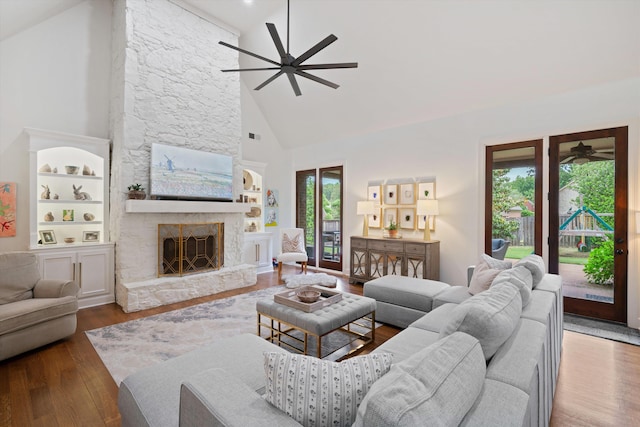 living room with built in shelves, ceiling fan, a stone fireplace, dark hardwood / wood-style flooring, and high vaulted ceiling