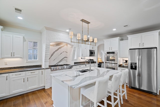 kitchen with decorative light fixtures, sink, stainless steel appliances, and an island with sink