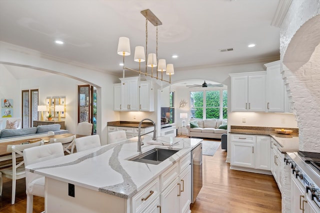 kitchen featuring white cabinetry, sink, light stone countertops, pendant lighting, and a kitchen island with sink