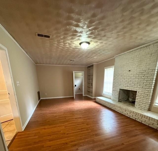 unfurnished living room with hardwood / wood-style floors, a textured ceiling, a brick fireplace, and ornamental molding