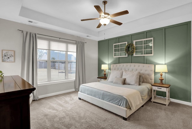 carpeted bedroom with a raised ceiling and ceiling fan