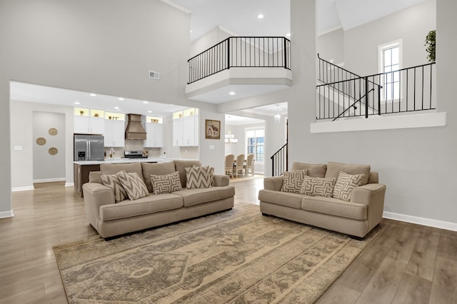 living room with light wood-type flooring, a towering ceiling, and an inviting chandelier