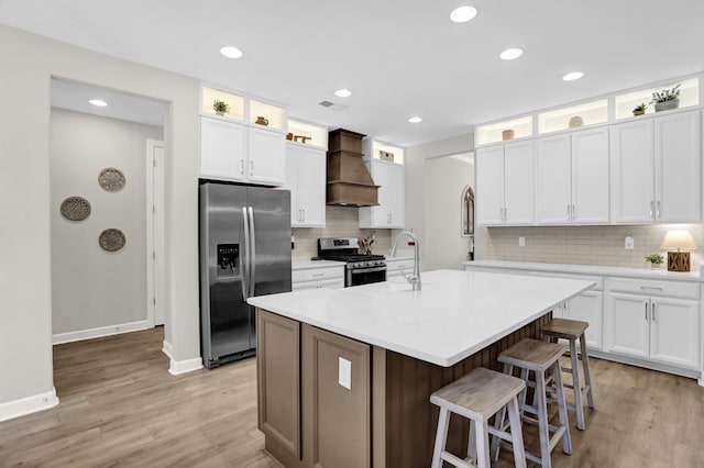 kitchen with a center island with sink, white cabinetry, custom range hood, and appliances with stainless steel finishes