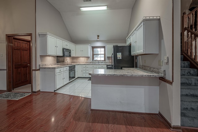 kitchen with kitchen peninsula, white cabinetry, black appliances, and light hardwood / wood-style floors