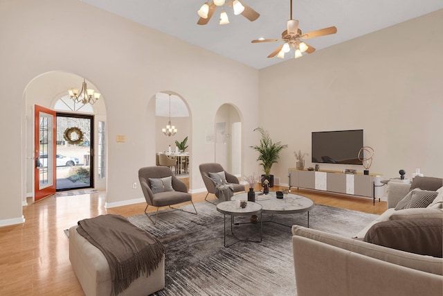 living room with ceiling fan with notable chandelier, light hardwood / wood-style floors, and a towering ceiling