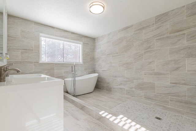 bathroom featuring a textured ceiling, a tub, sink, and tile walls