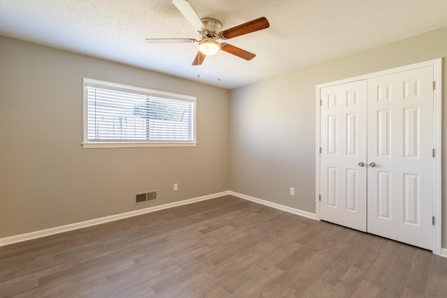 unfurnished bedroom with ceiling fan, wood-type flooring, a textured ceiling, and a closet