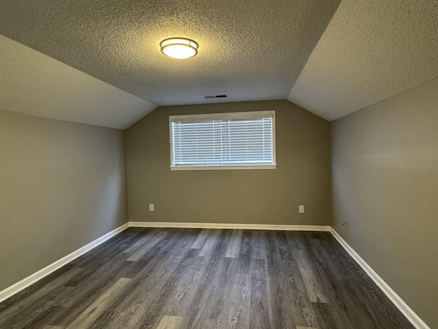 additional living space featuring dark hardwood / wood-style flooring, a textured ceiling, and vaulted ceiling