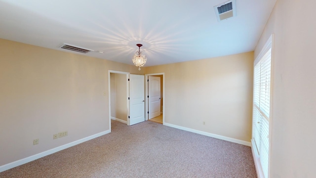 empty room with light colored carpet and a chandelier