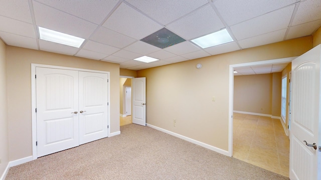 unfurnished bedroom featuring a paneled ceiling, light colored carpet, and a closet