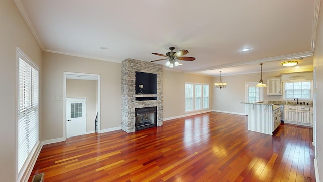 unfurnished living room featuring sink, dark hardwood / wood-style flooring, crown molding, a fireplace, and ceiling fan with notable chandelier