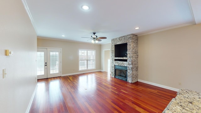 unfurnished living room with ceiling fan, a stone fireplace, ornamental molding, and french doors