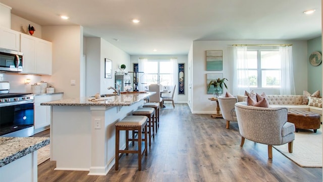 kitchen featuring stainless steel appliances, open floor plan, white cabinets, and a kitchen bar