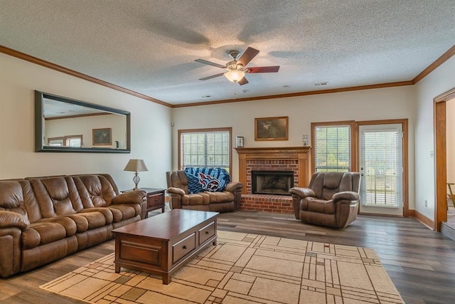 living room with a brick fireplace, a textured ceiling, ceiling fan, crown molding, and wood-type flooring